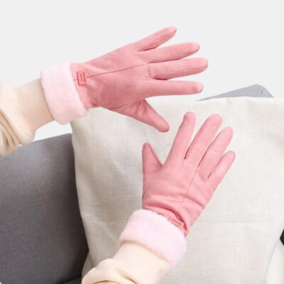 Gants rose en daim de coton sur des mains au dessus d'un coussin.