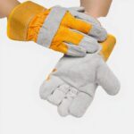 2 mains gantées en gris et jaune. Une main la paume tournéee vers le haut et l'autre posée sur le poignet de l'autre
