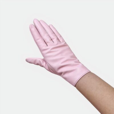 Photo d'une main de femme portant un gant court rose en cuir très élégant au dessus d'un morceau de cuir blanc froissé