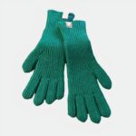Photo d'une paire de gants verts en laine en grosse maille posés sur un plat en bambou lui-même sur une table en bois clair, un bout de magazine au papier glacé à droite