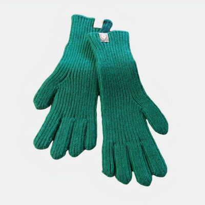 Photo d'une paire de gants verts en laine en grosse maille posés sur un plat en bambou lui-même sur une table en bois clair, un bout de magazine au papier glacé à droite