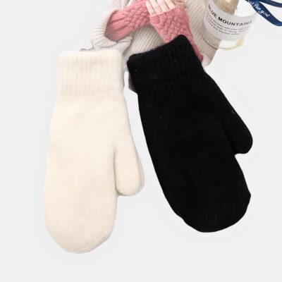 Photo de deux gants style moufles en laine et cachemire, l'un blanc et l'autre noir sur un tissu blanc et un magazine de mode avec un flacon de senteur sur la droite