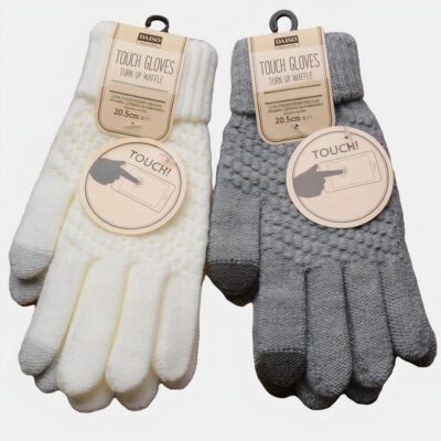 Photo montrant deux paires de gants d'hiver en tricot l'une blanche et l'autre grise avec bouts du pouce et de l'index permettant une utilisation des écrans tactiles, elles sont posés sur une planchette de bois et sur un fond marron clair