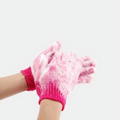 mains dans une paire de gants exfoliants rose foncé avec mousse